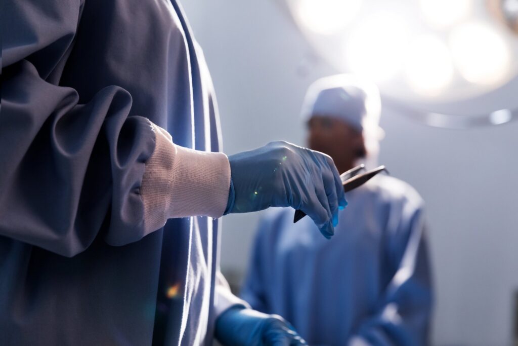 Chirurg z pęsetą w dłoni w rękawiczce.